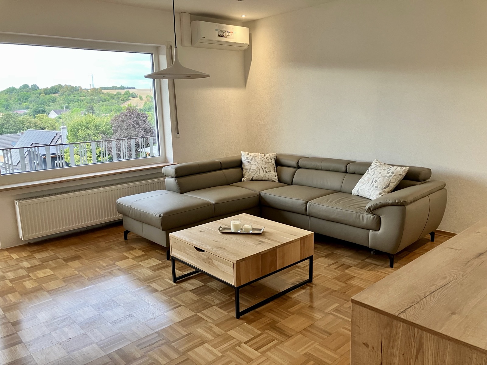 Helles Wohnzimmer mit großer Eckcouch, Klimaanlage und Aussicht ins Grüne im Ferienhaus Obersfeld